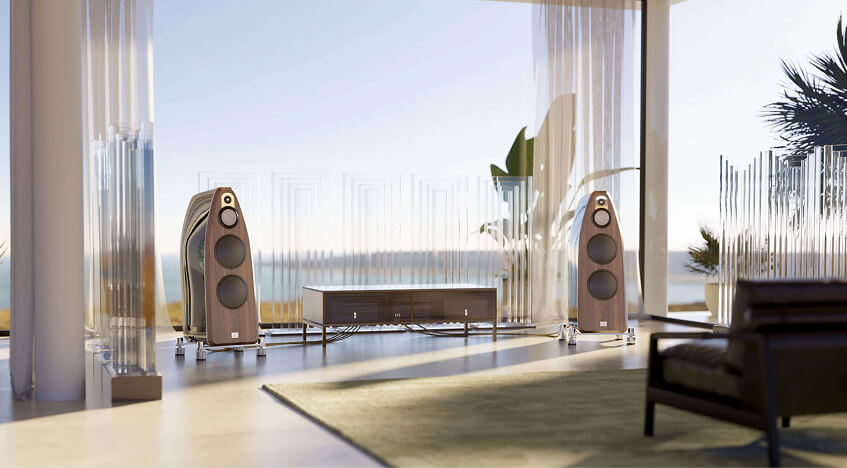 Modern living room with large speakers, a low table, glass walls, and a view of the ocean in the background.